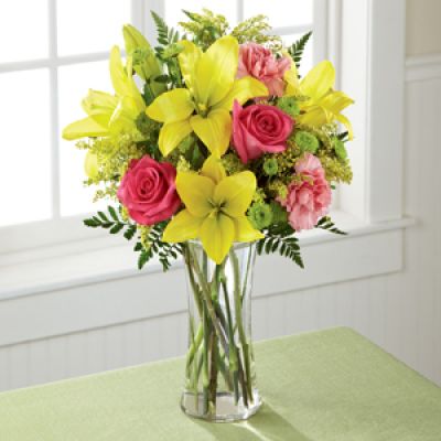 Light, lovely, and set to surprise and delight your recipient with it's bright blooms, this flower bouquet speaks to the magic that each day holds. Brilliant yellow Asiatic Lilies are surrounded by hot pink roses, pink carnations, yellow solidago, and lush greens, beautifully arranged in a classic clear glass vase to create a gift that exudes warmth and happiness. A wonderful way to celebrate a birthday, or express your thank you, or congratulations wishes!